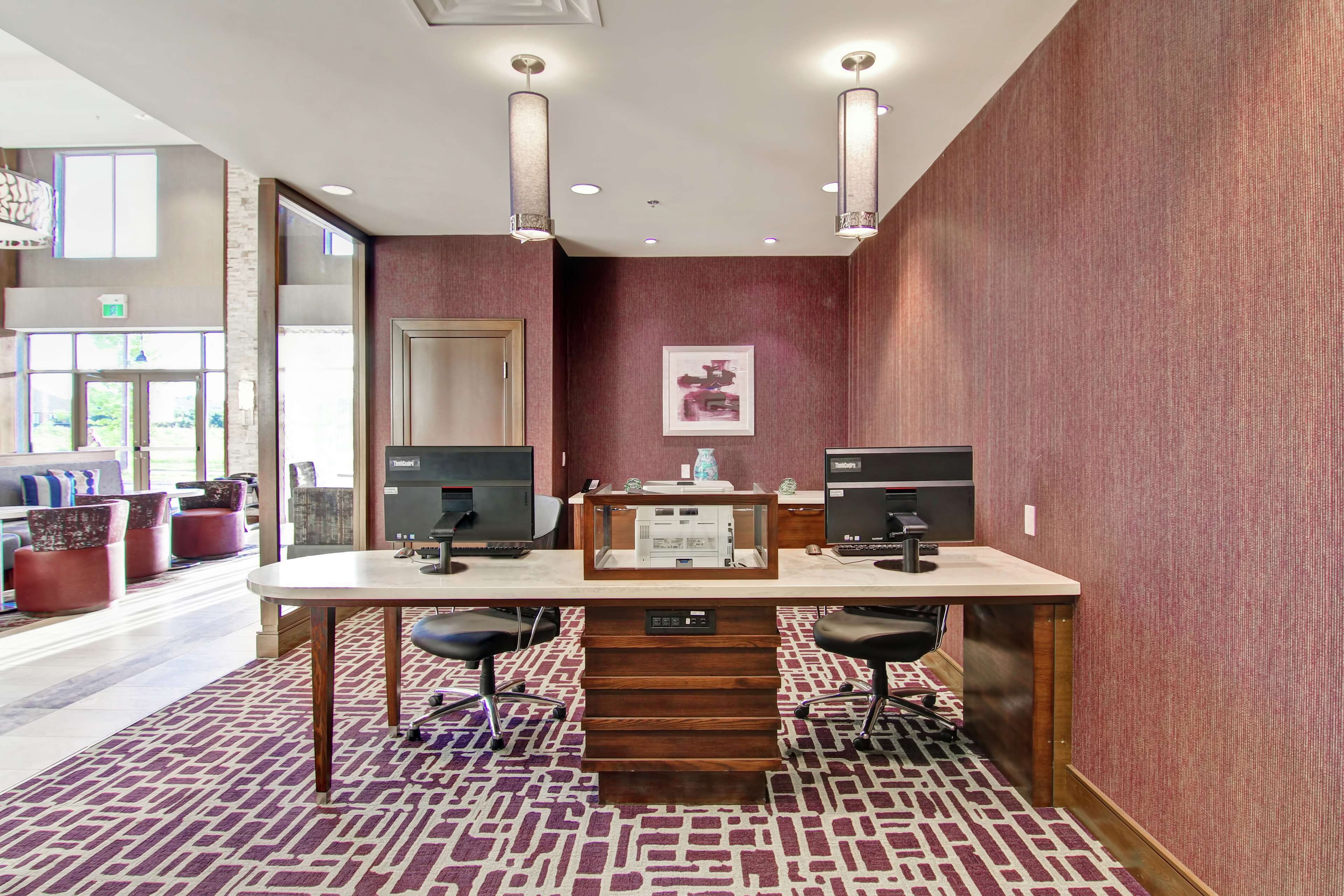 Un vestíbulo de hotel con una recepción, dos estaciones de computadora y una zona de estar con sillas y pufs.