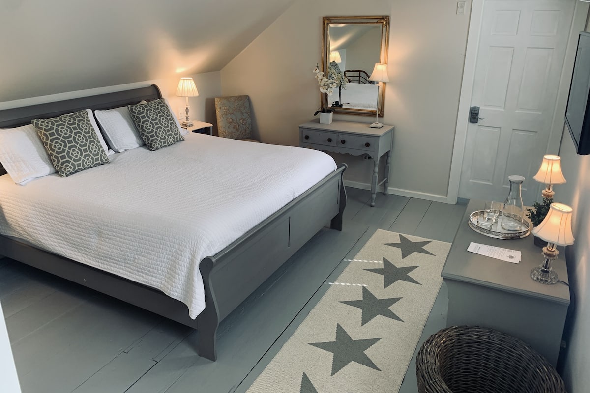 Ein Schlafzimmer mit einem Bett, Nachttischen, einer Kommode, einem Spiegel und einer Tür.