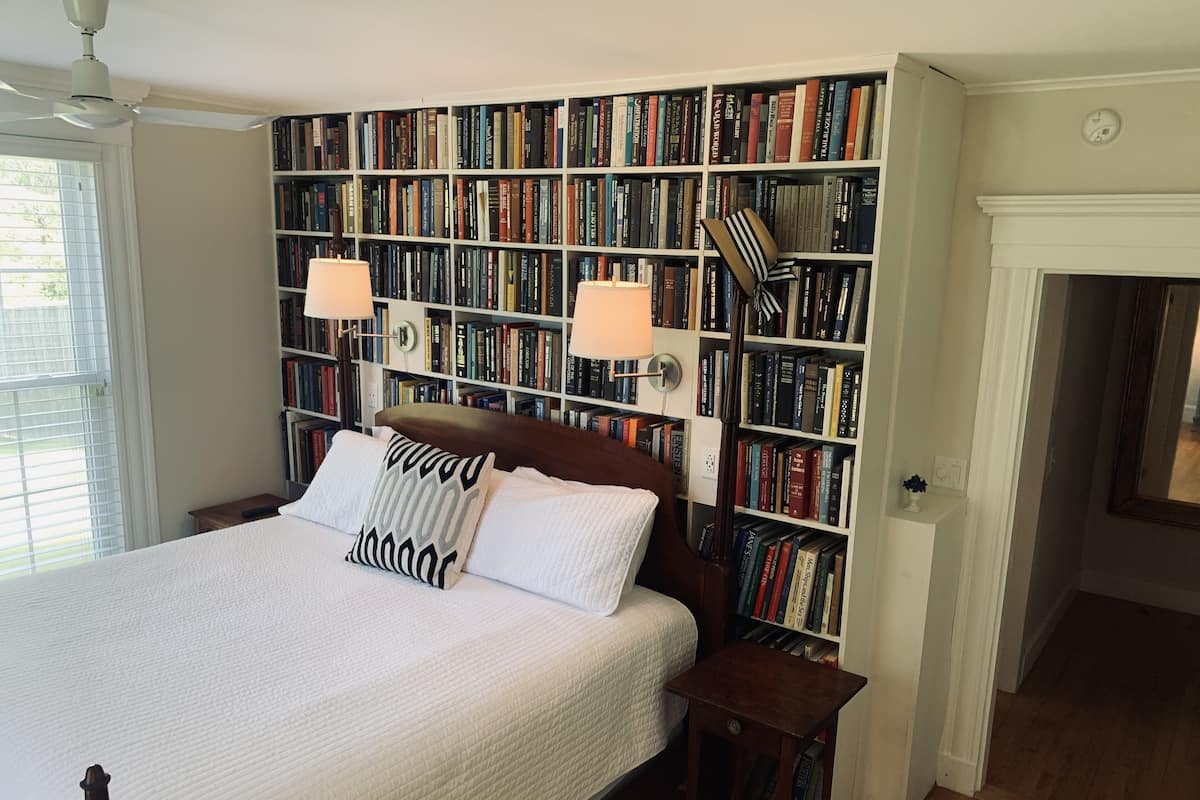 Ein Schlafzimmer mit einer großen Bücherwand, einem Bett mit weißer Bettwäsche und zwei Nachttischlampen.