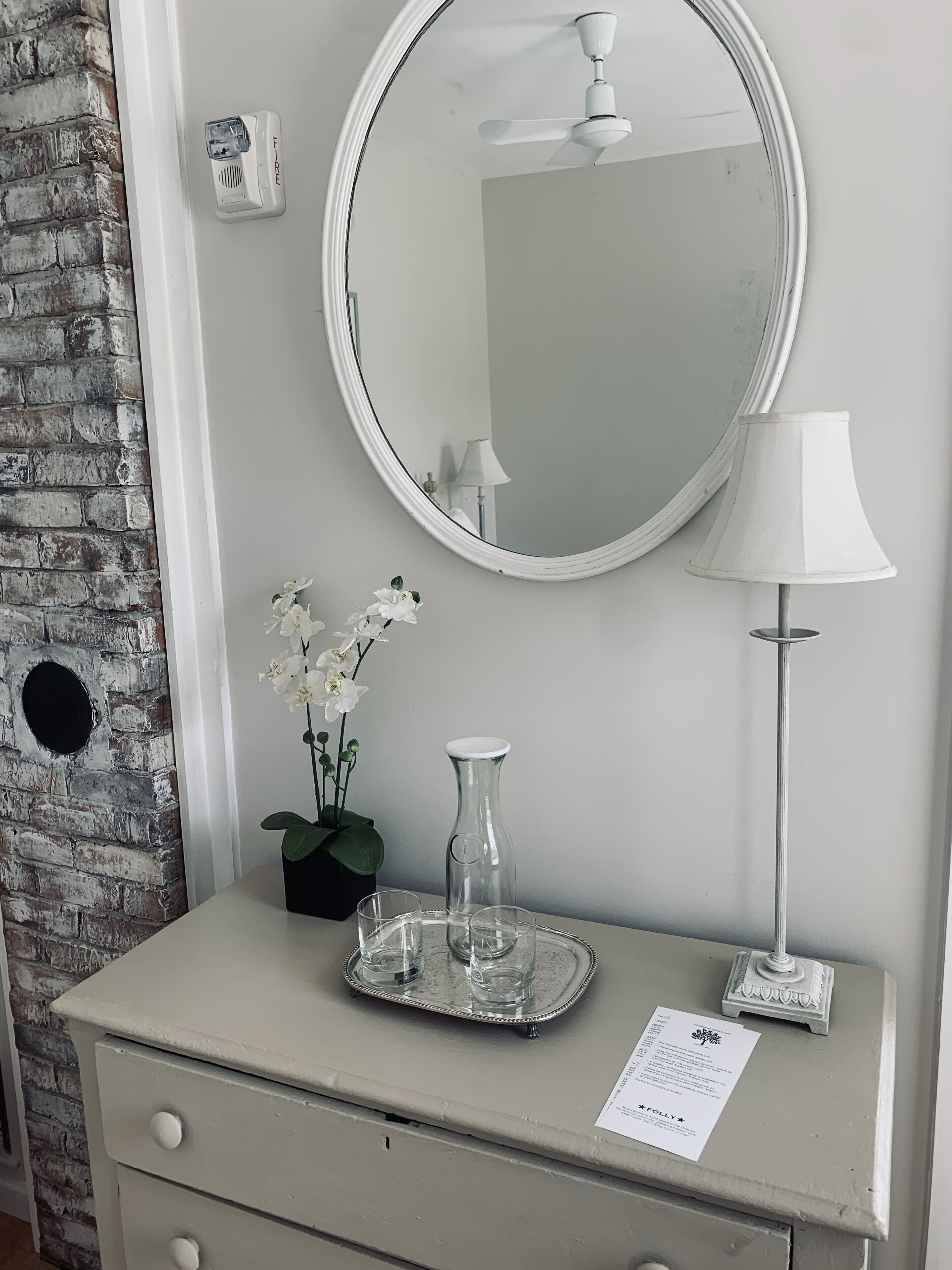 A bathroom vanity with a mirror, a lamp, a vase with flowers, and a tray with glasses.