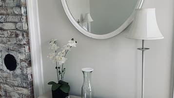 A bathroom vanity with a mirror, a lamp, a vase with flowers, and a tray with glasses.