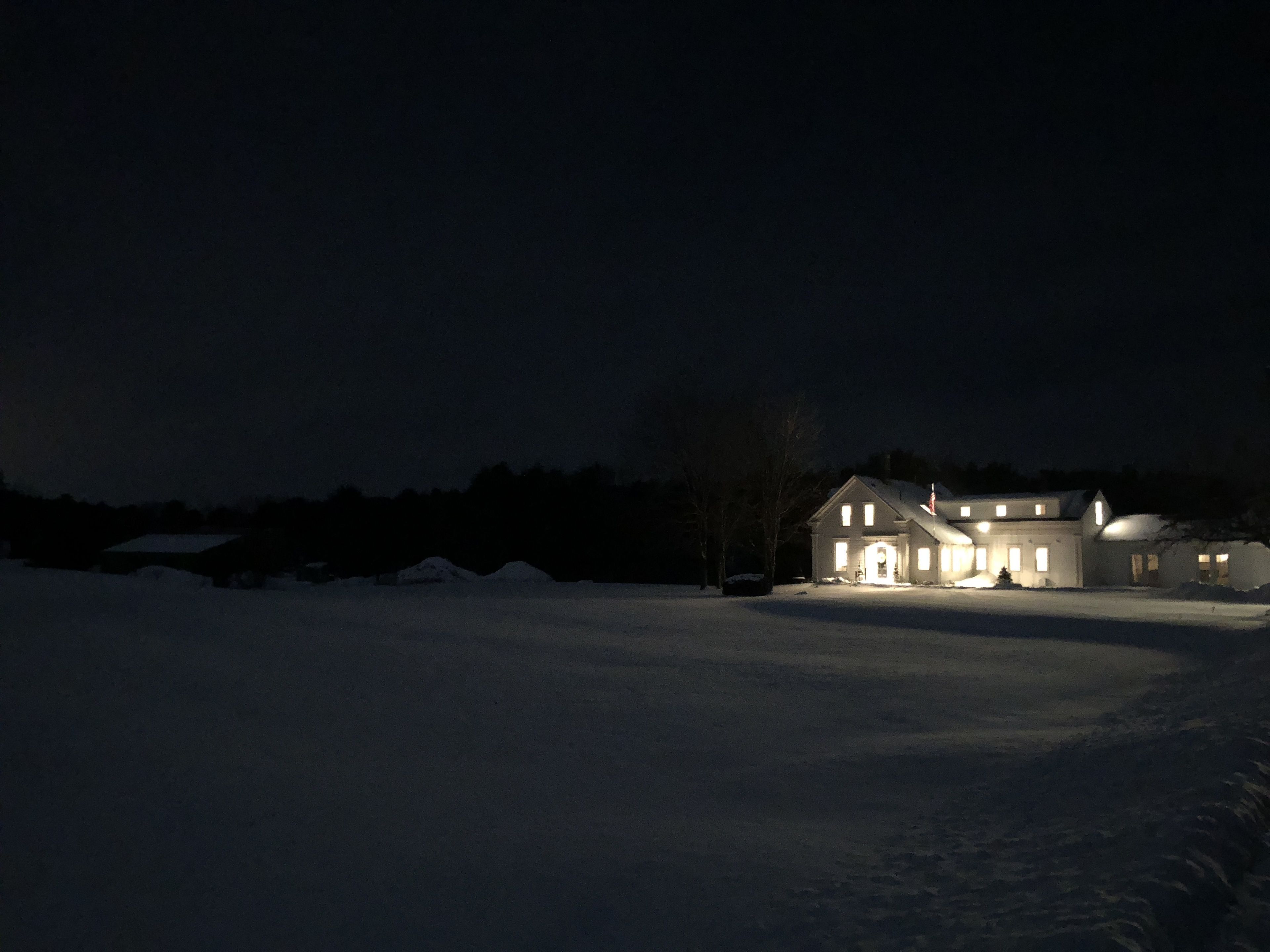 A large, illuminated house with a snow-covered driveway at night.