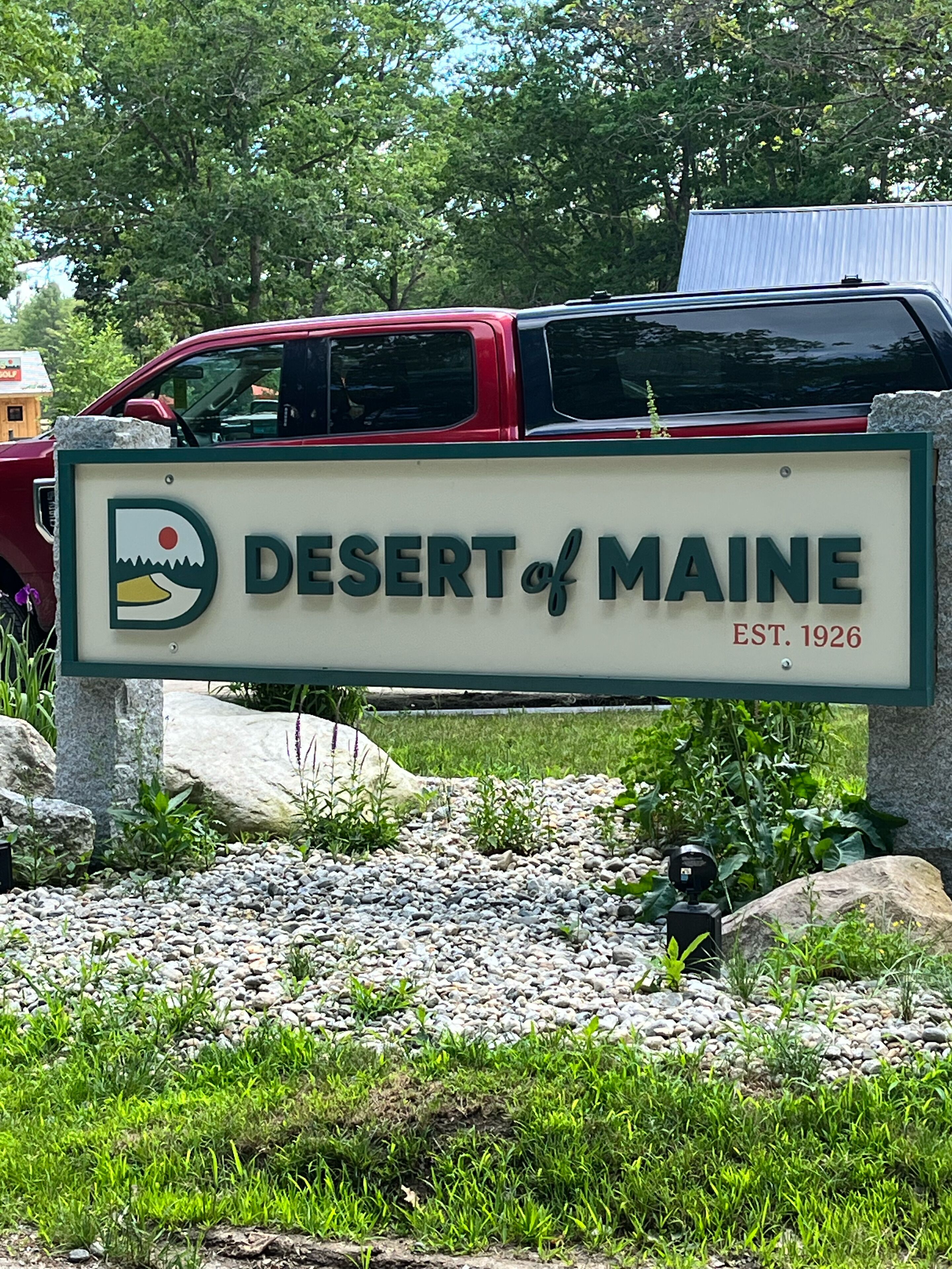 A sign for the Desert of Maine, established in 1926, with a logo featuring a mountain and sun.