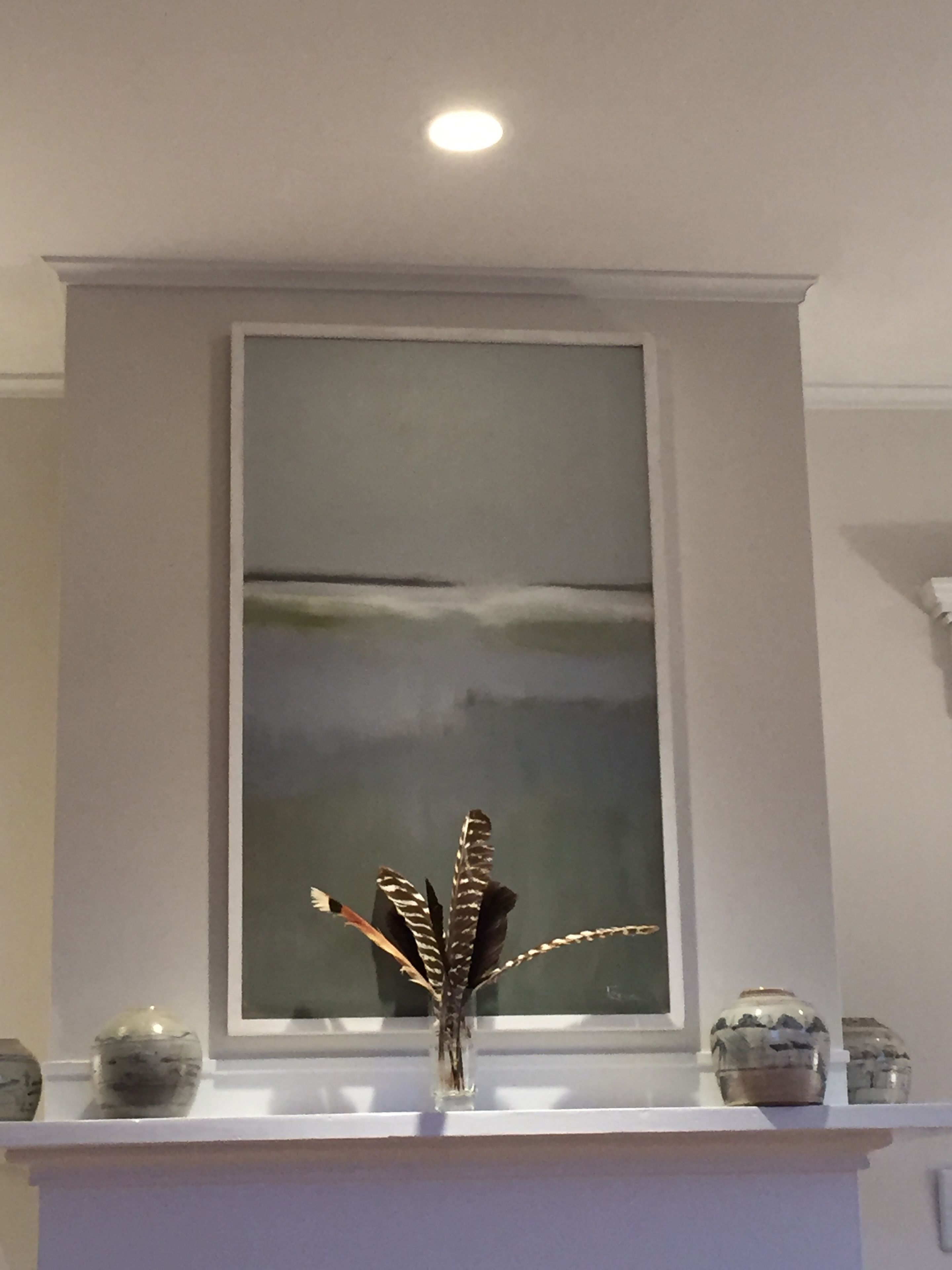 A room with a white mantelpiece, a framed abstract painting, and a vase with decorative elements.
