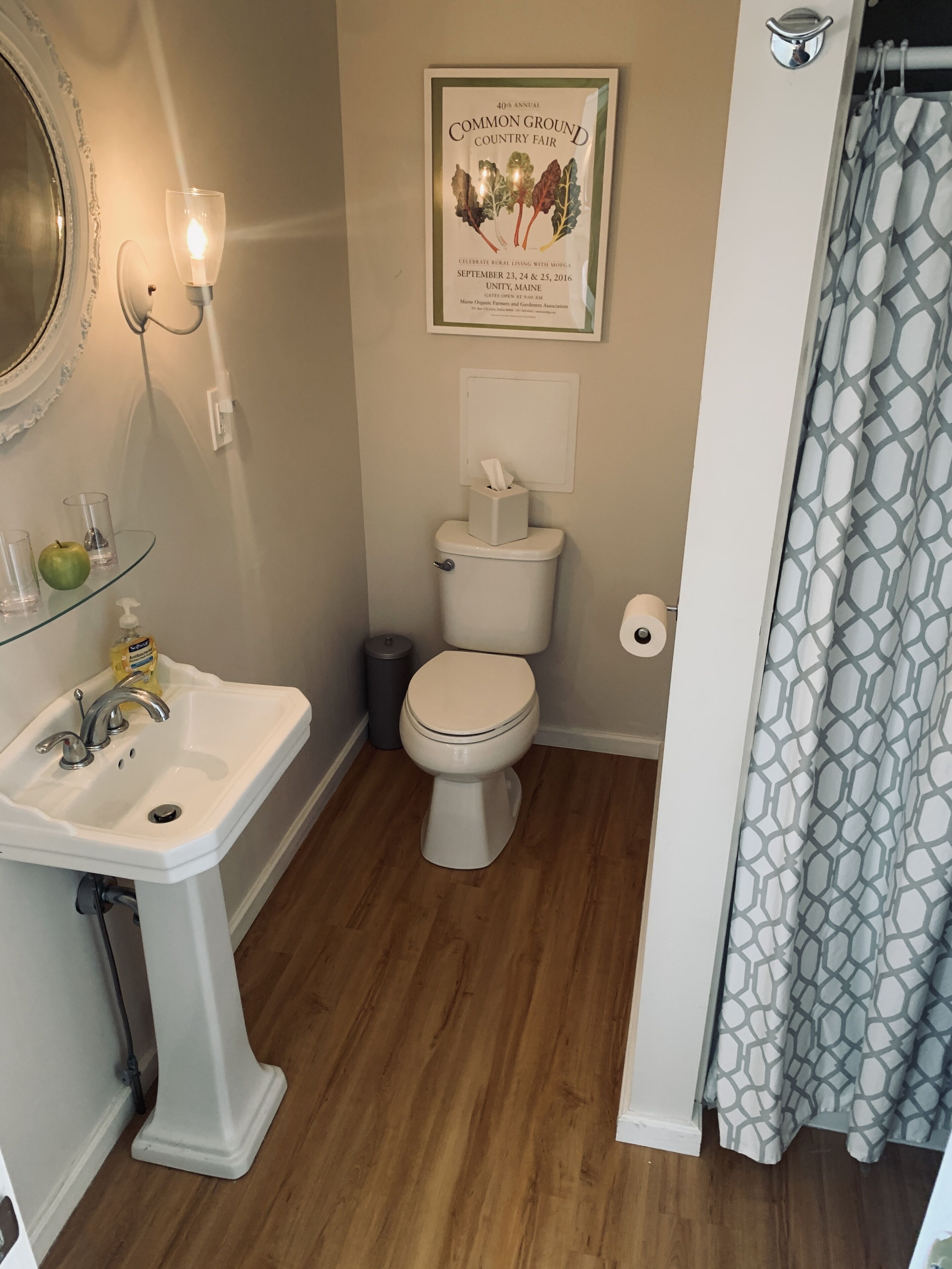 A bathroom with a pedestal sink, toilet, and a framed sign on the wall.