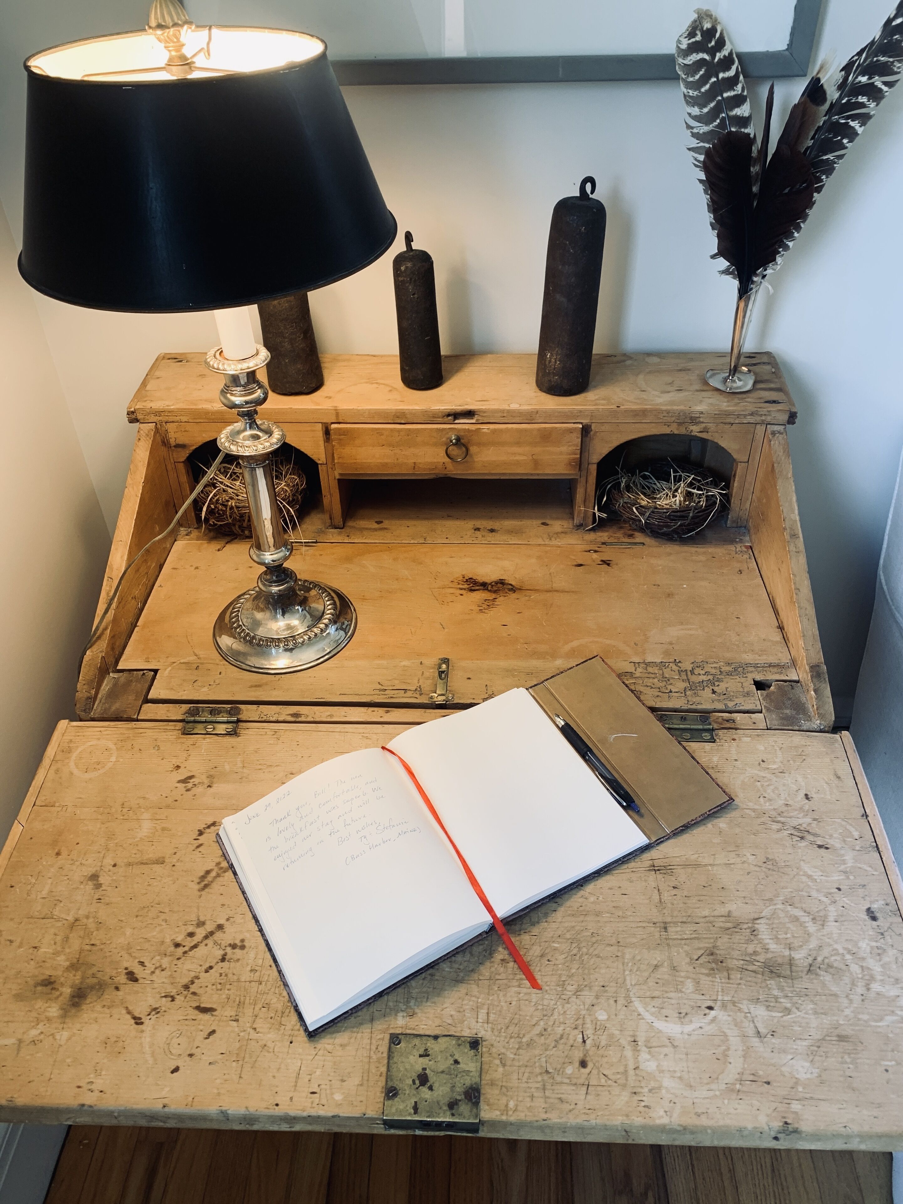A rustic wooden desk with a lamp, a candle holder, and a decorative feather.