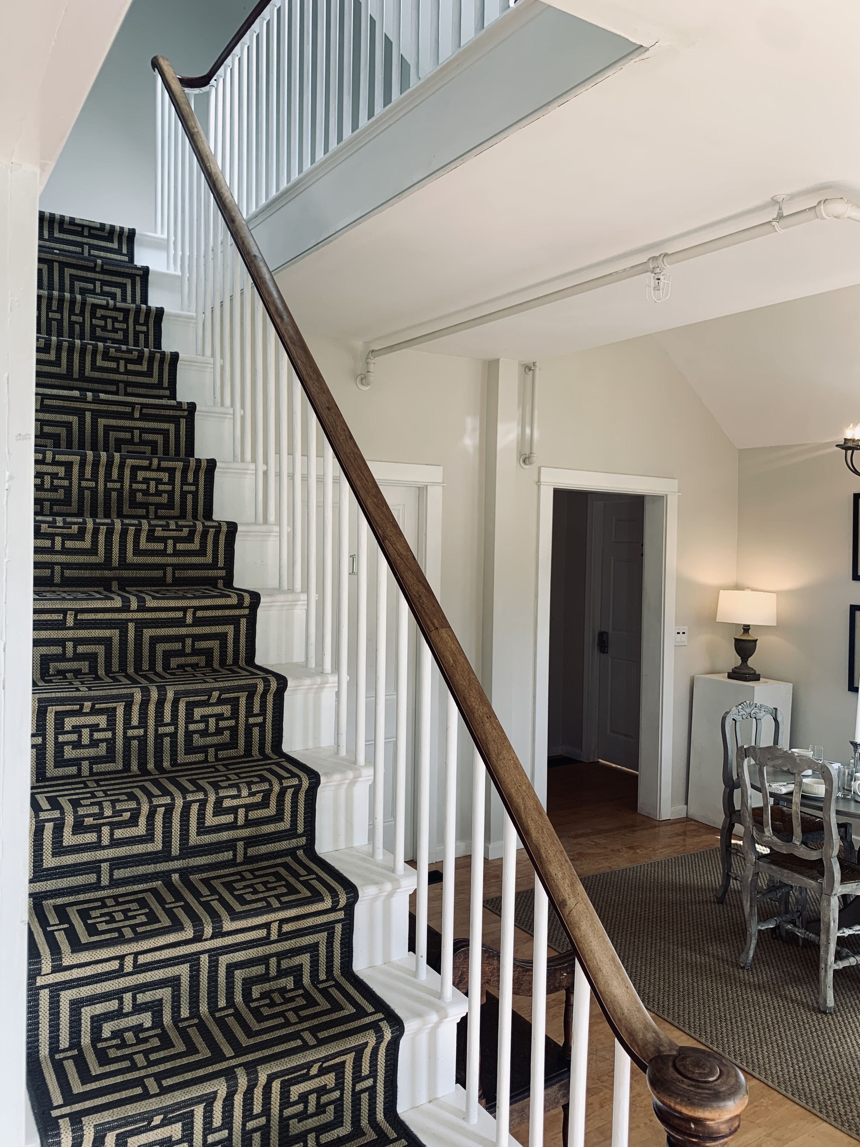 A staircase with a geometric patterned carpet, white railings, and a wooden handrail.