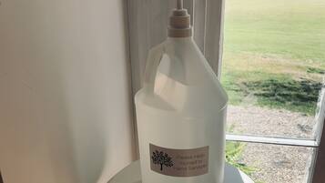 A hand sanitizer bottle on a pedestal table near a window with a view of a grassy area.