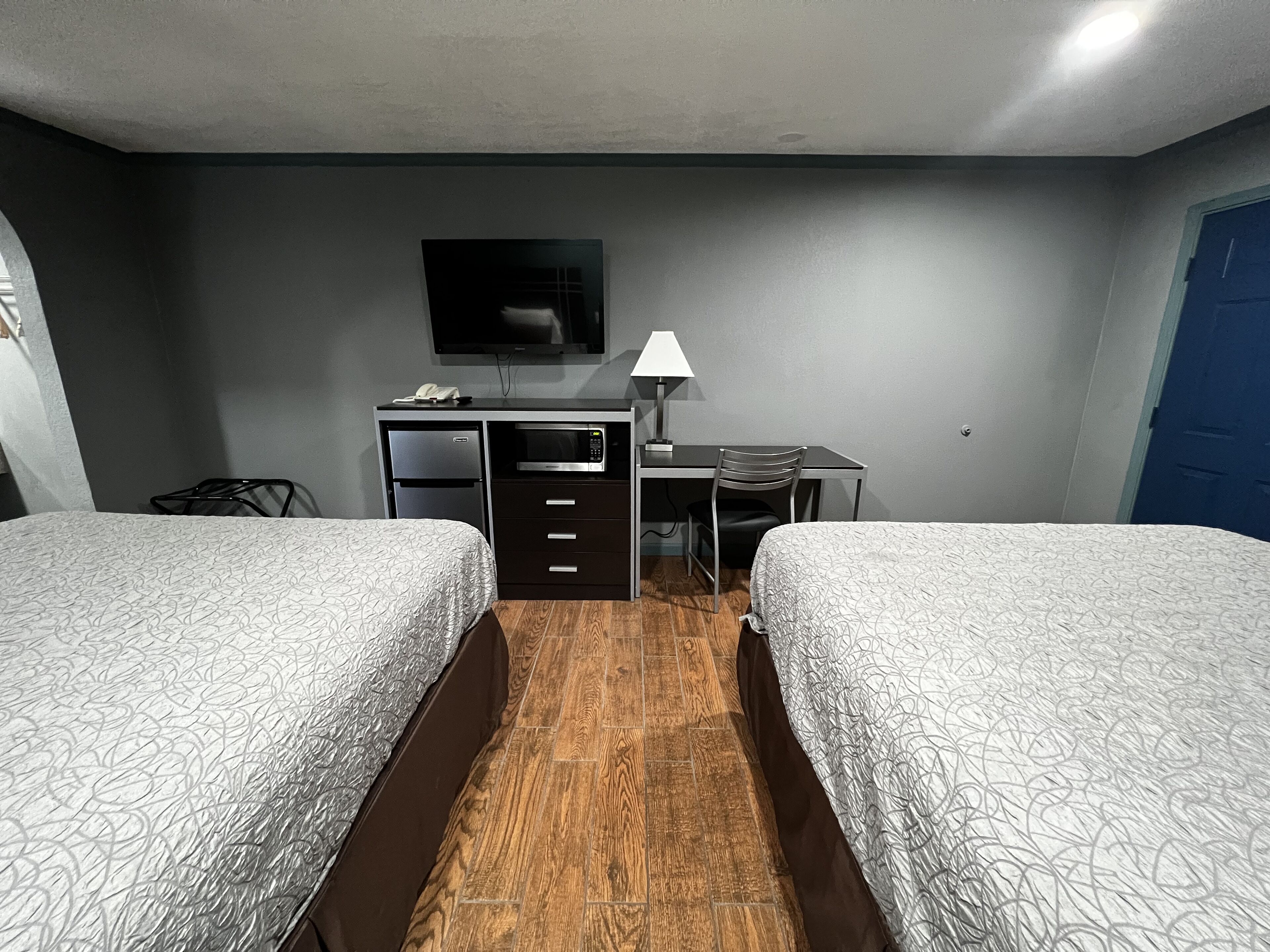A hotel room with two beds, a desk, a chair, a TV, and a lamp.