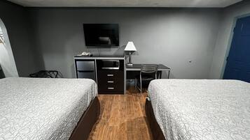 A hotel room with two beds, a desk, a chair, a TV, and a lamp.