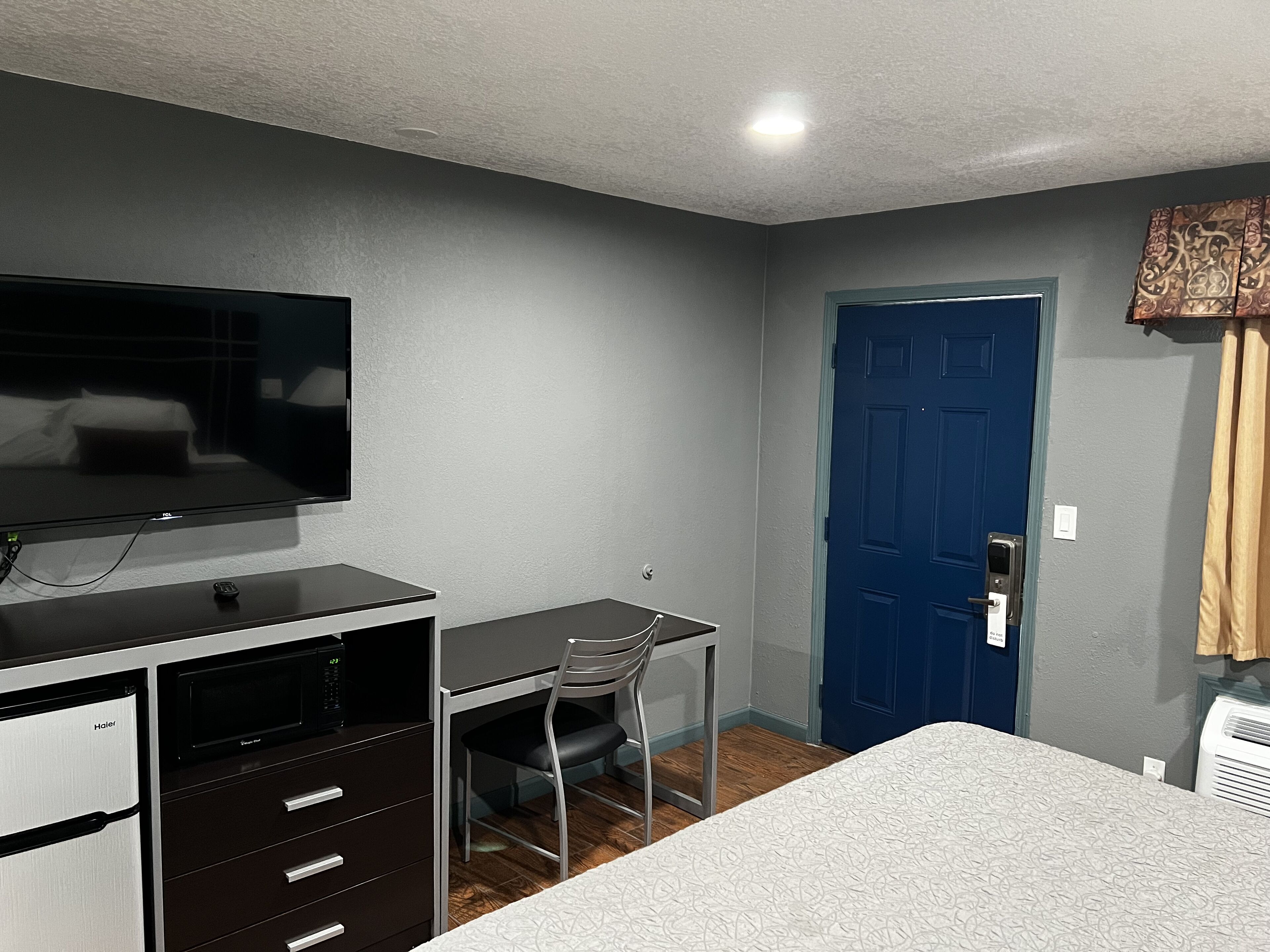 Habitación de hotel con cama, escritorio con silla, televisor, armario y una puerta azul.