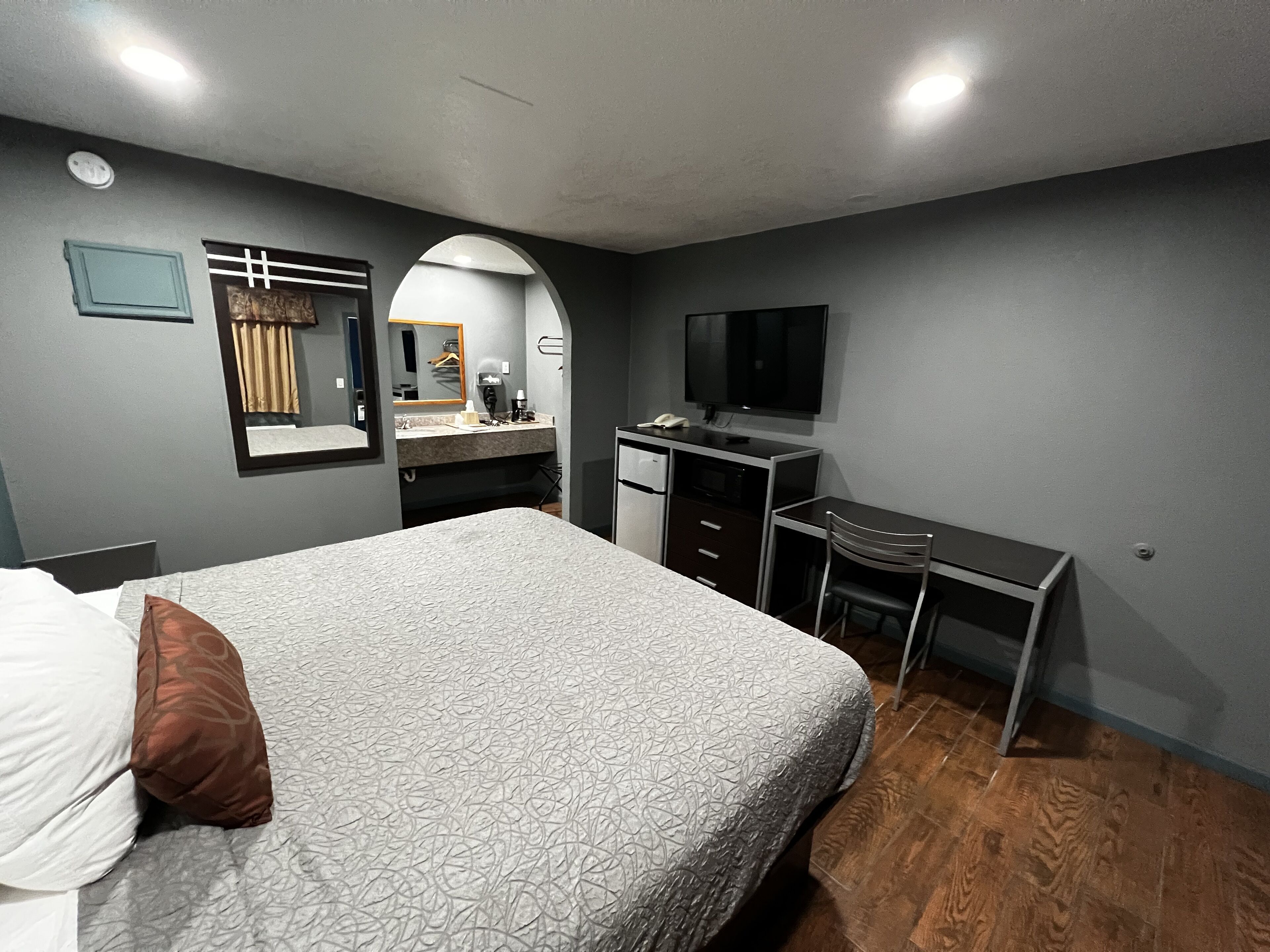 A bedroom with a bed, a desk, a chair, a TV, and a mirror.