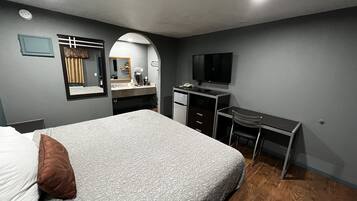 A bedroom with a bed, a desk, a chair, a TV, and a mirror.