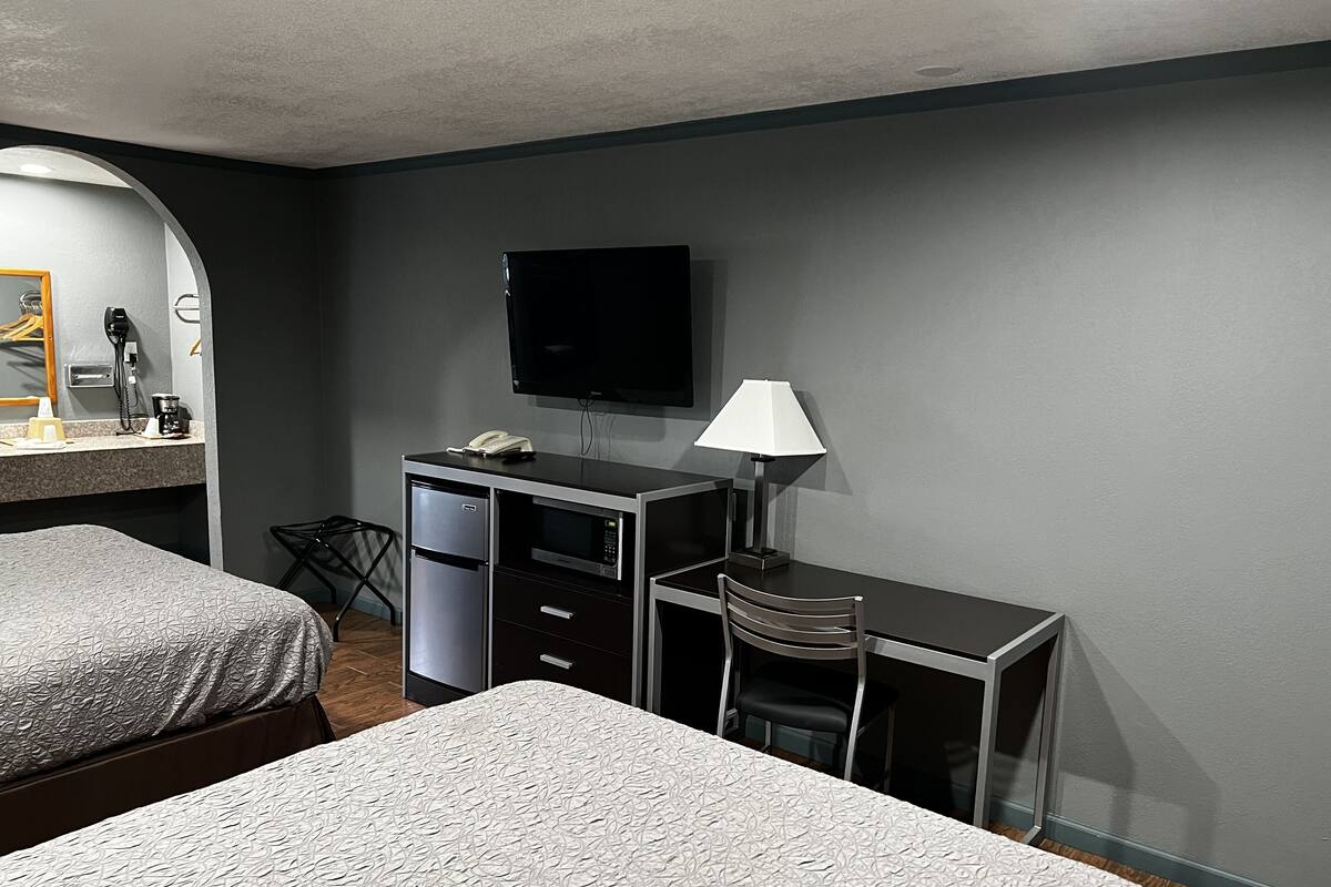 A hotel room with two beds, a desk with a chair, a TV, a lamp, and a minibar.