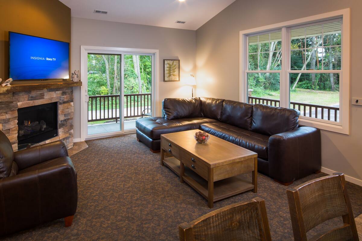 A living room with a stone fireplace, leather sofa, and a flat-screen TV.