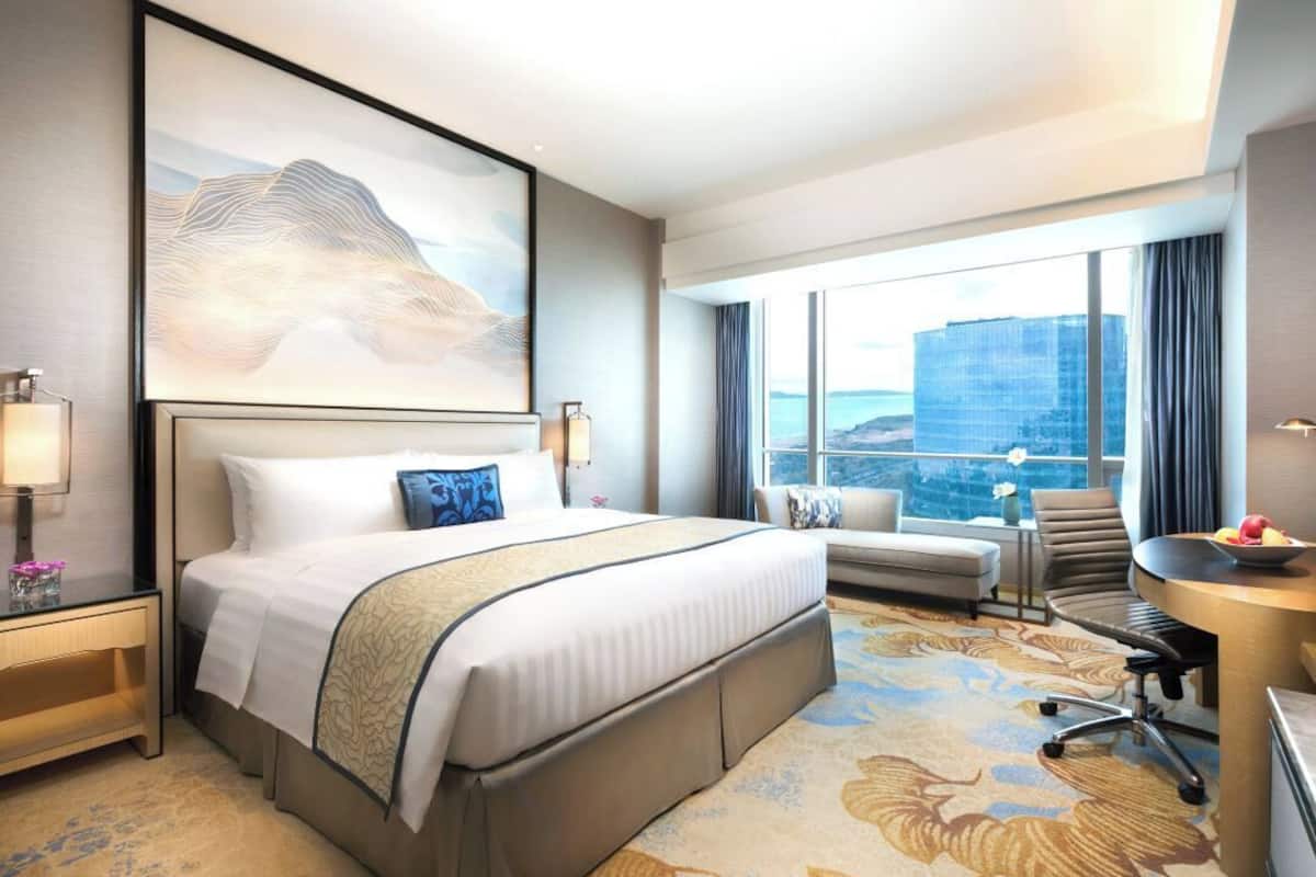 Une chambre d’hôtel avec un grand lit, un bureau, une chaise et une vue sur le paysage urbain, grâce à de grandes fenêtres.