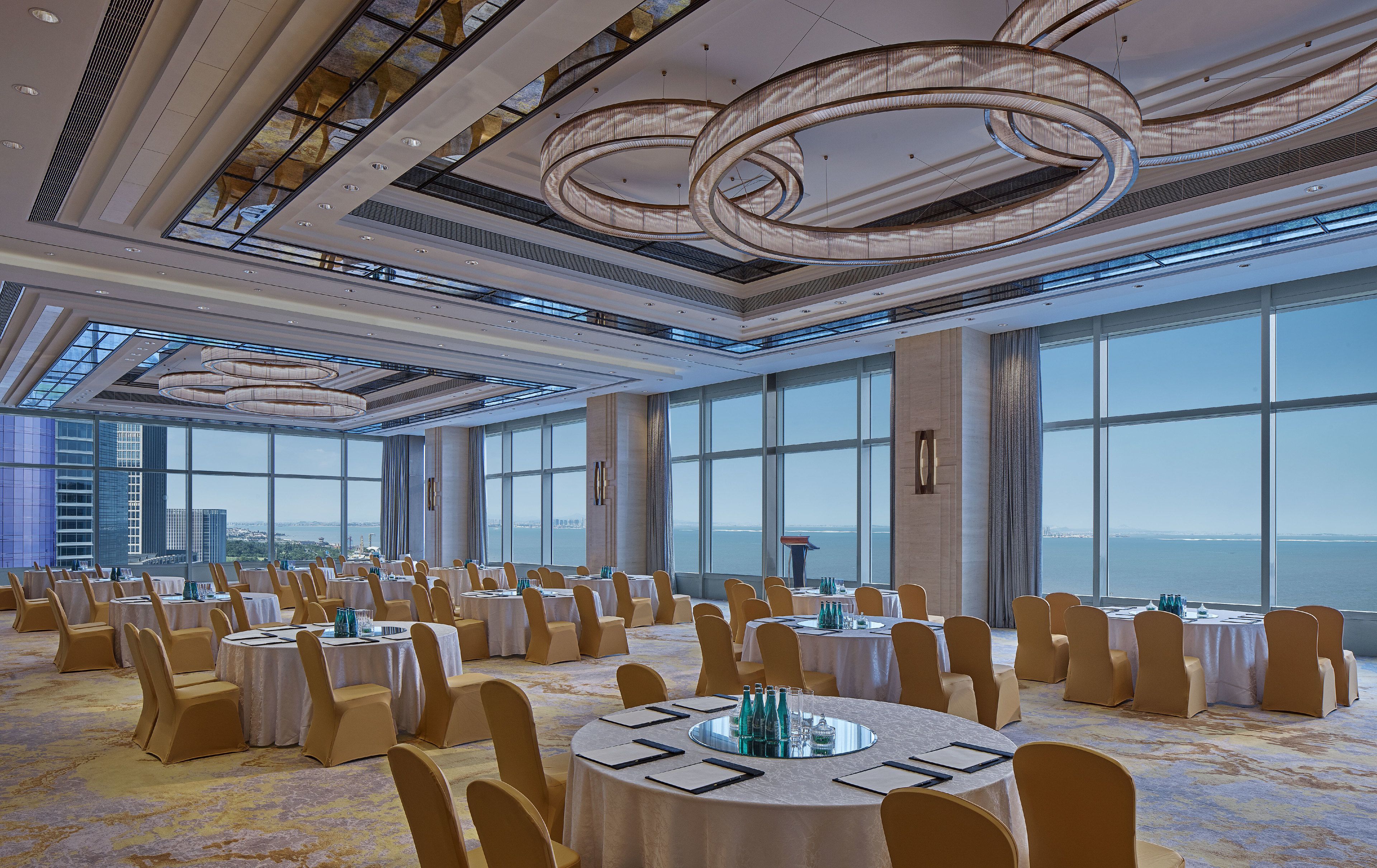Un amplio salón de banquetes con mesas redondas, sillas y vistas panorámicas de la ciudad y el agua.