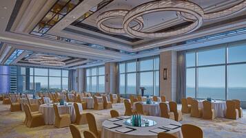 Un amplio salón de banquetes con mesas redondas, sillas y vistas panorámicas de la ciudad y el agua.