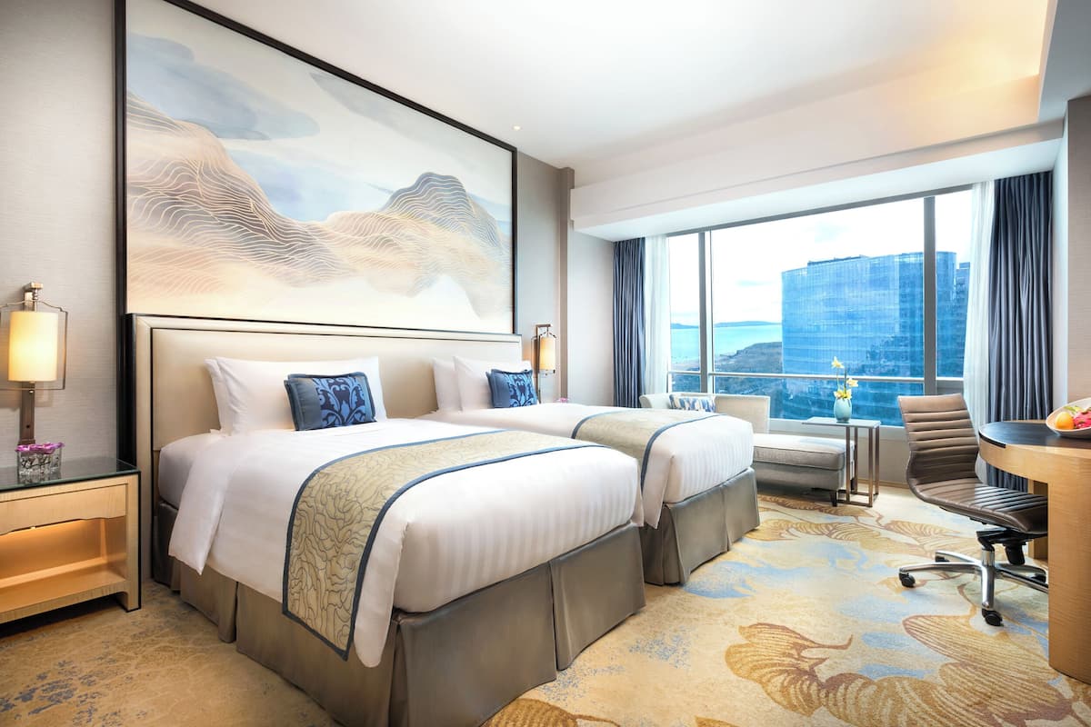 Une chambre d’hôtel avec deux lits, un bureau et une grande fenêtre donnant sur la ville.