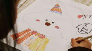 A person drawing on a white tote bag with a face design, including a hat and a heart with text.