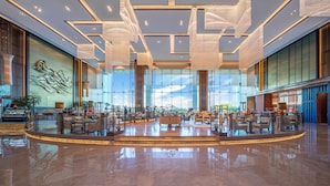 Een ruime lobby met een centraal zithoek, grote ramen en moderne kroonluchters.