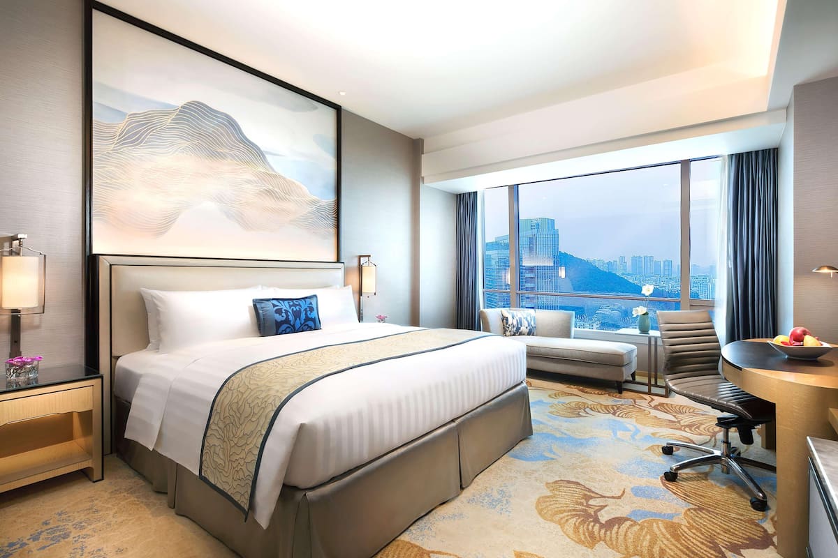 Une chambre d’hôtel avec un grand lit, un bureau, une chaise, une vue sur le paysage urbain et une grande œuvre d’art accrochée au mur.