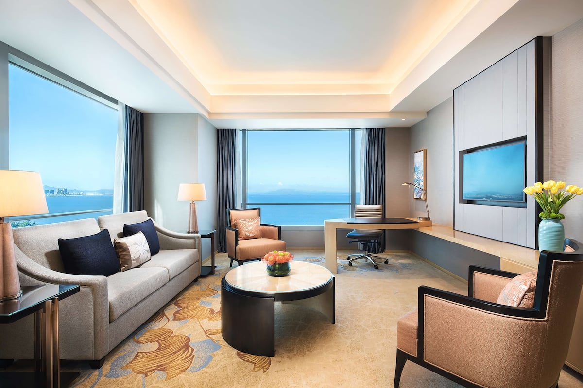 Une chambre d’hôtel moderne équipée d’un canapé, d’un fauteuil, d’une table basse et d’un bureau avec un téléviseur.