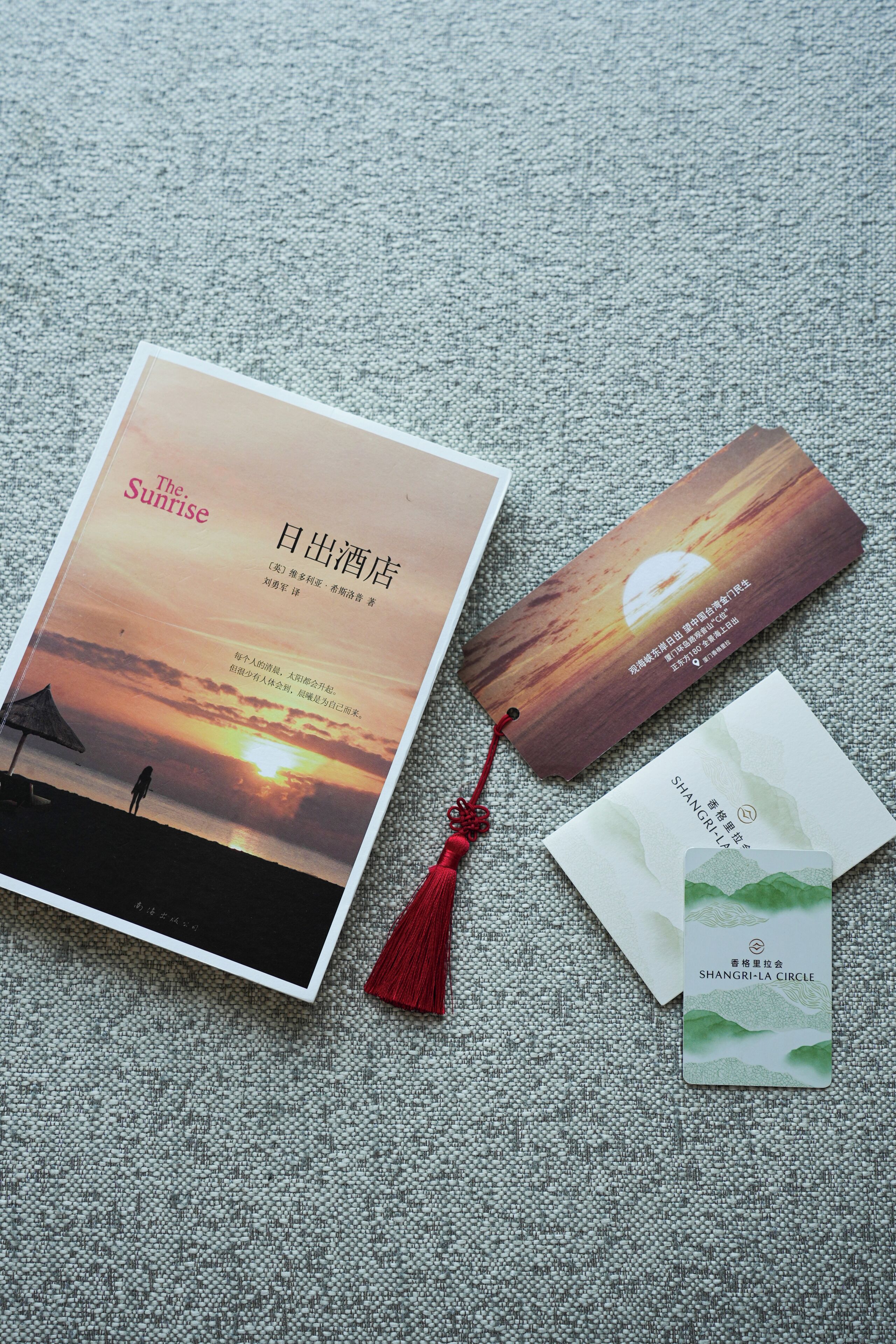 A book titled 'The Sunrise' with a sunset image on the cover, a bookmark, and two business cards.