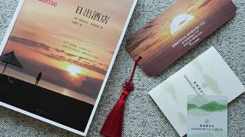 A book titled 'The Sunrise' with a sunset image on the cover, a bookmark, and two business cards.