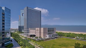 Een modern gebouw met een glazen gevel, direct grenzend aan een strand, met een verzorgd gazon en een helder uitzicht op de oceaan.