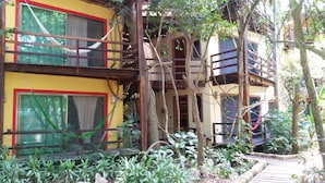 A multi-story building with a balcony, surrounded by lush greenery and a wooden deck. - Dolce Caribe B&B (Playa del Carmen)