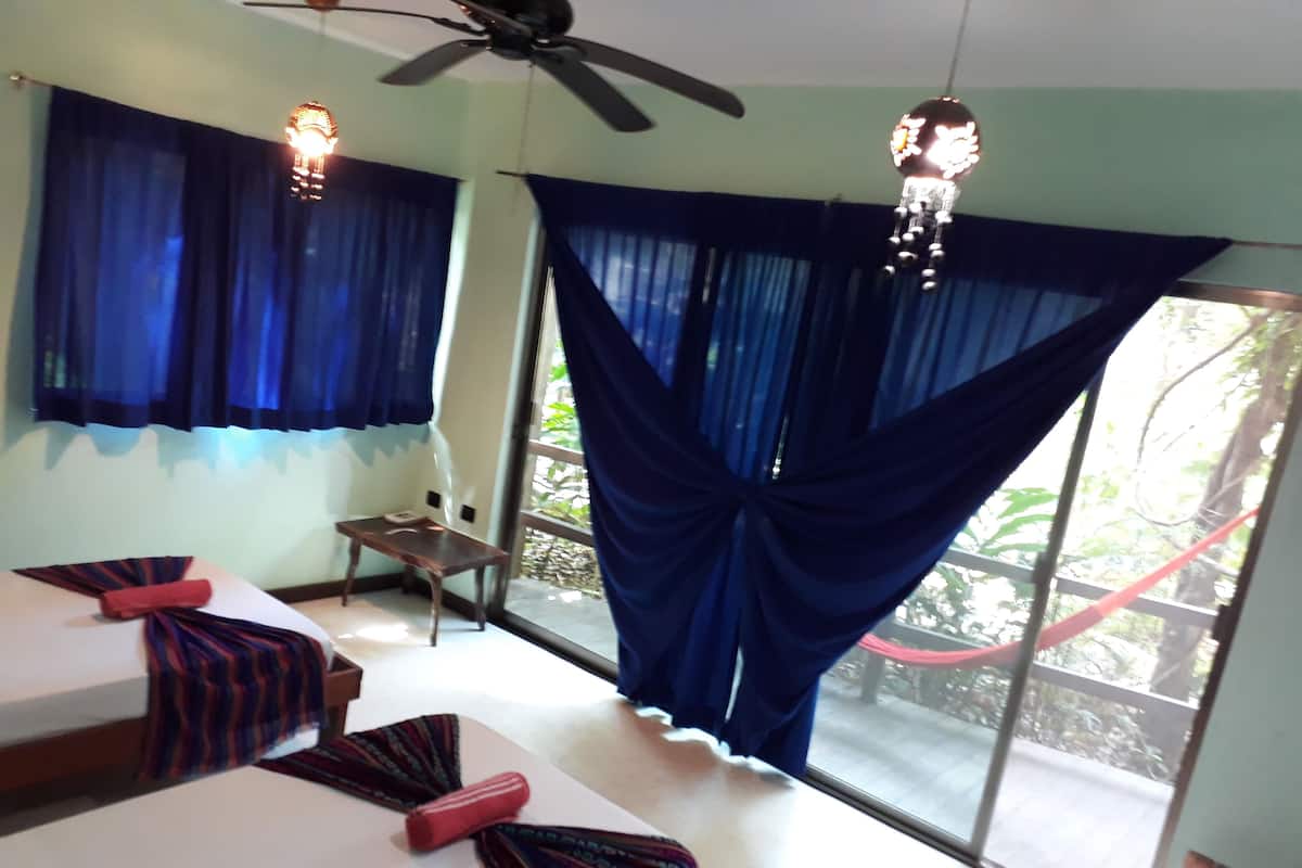 Ein Zimmer mit zwei Betten, einem Deckenventilator und großen Fenstern mit blauen Vorhängen.