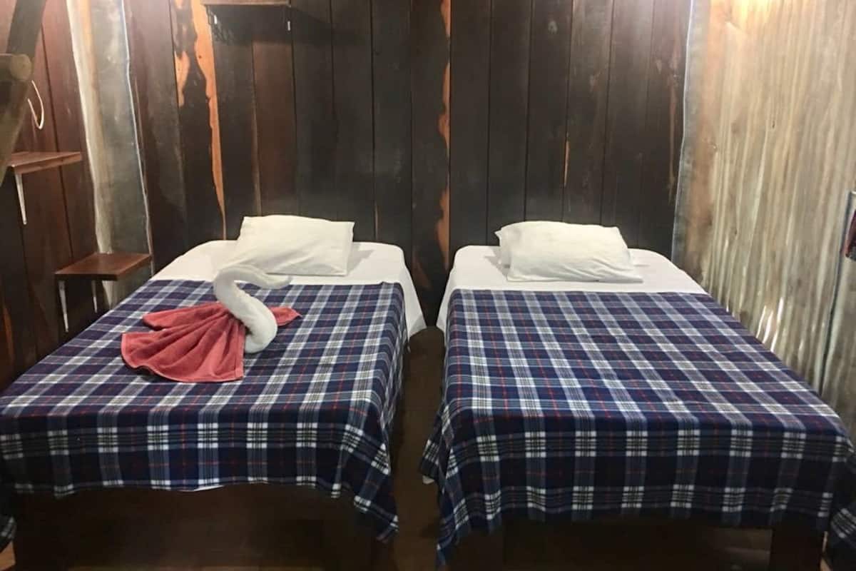 Zwei Einzelbetten mit karierter Bettwäsche, ein schwanenförmiges Kopfkissen und ein pinkfarbenes Handtuch auf einem Bett.