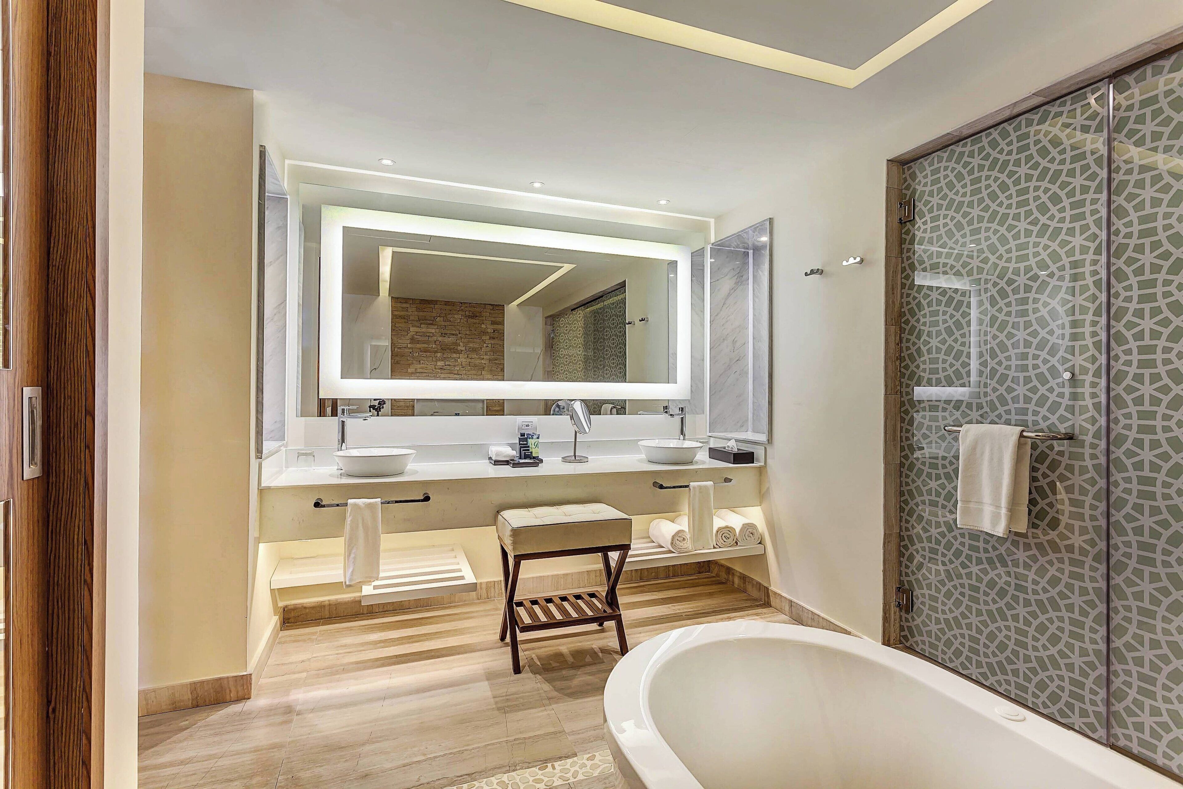 A modern bathroom with a large mirror, two sinks, a bathtub, and a glass shower enclosure.