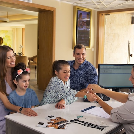 A family of four seated at a table in a well-lit room with a modern interior, a computer monitor, and documents on the table.