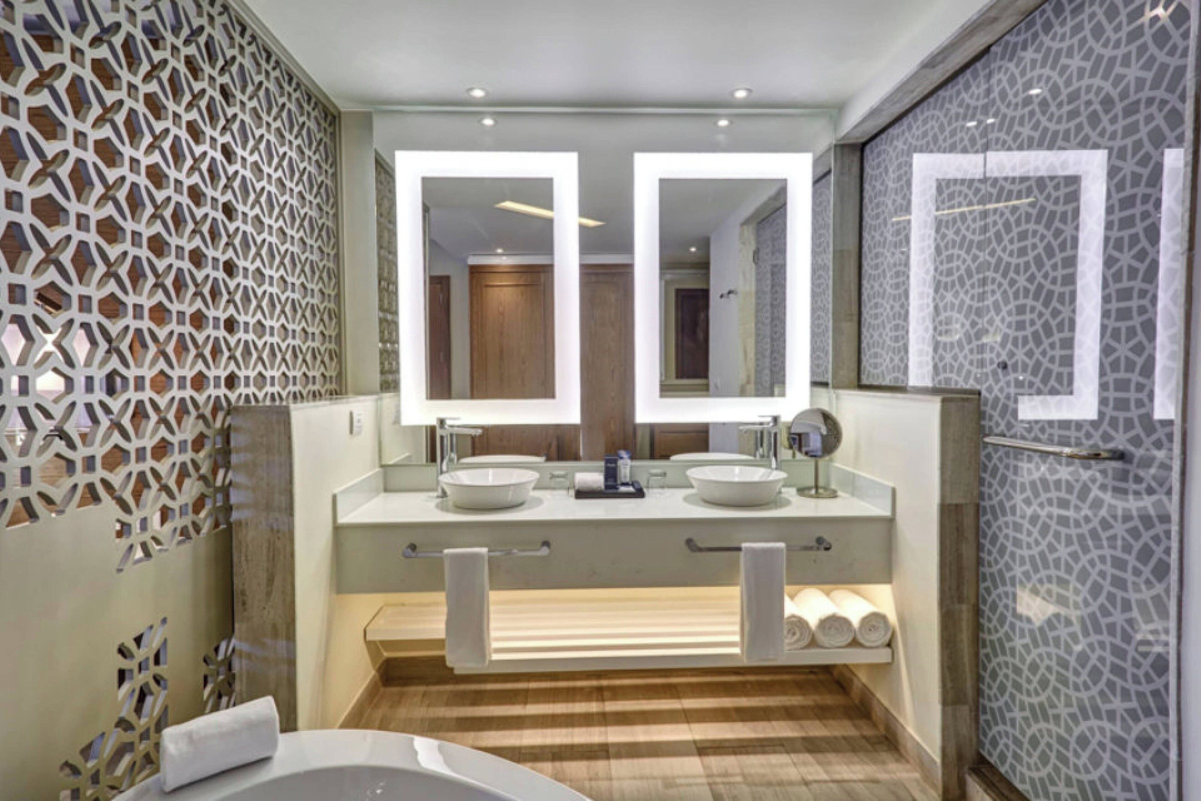 A modern bathroom with a large mirror, two sinks, a bathtub, and a shower area.