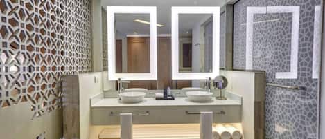 A modern bathroom with a large mirror, two sinks, a bathtub, and a shower area.