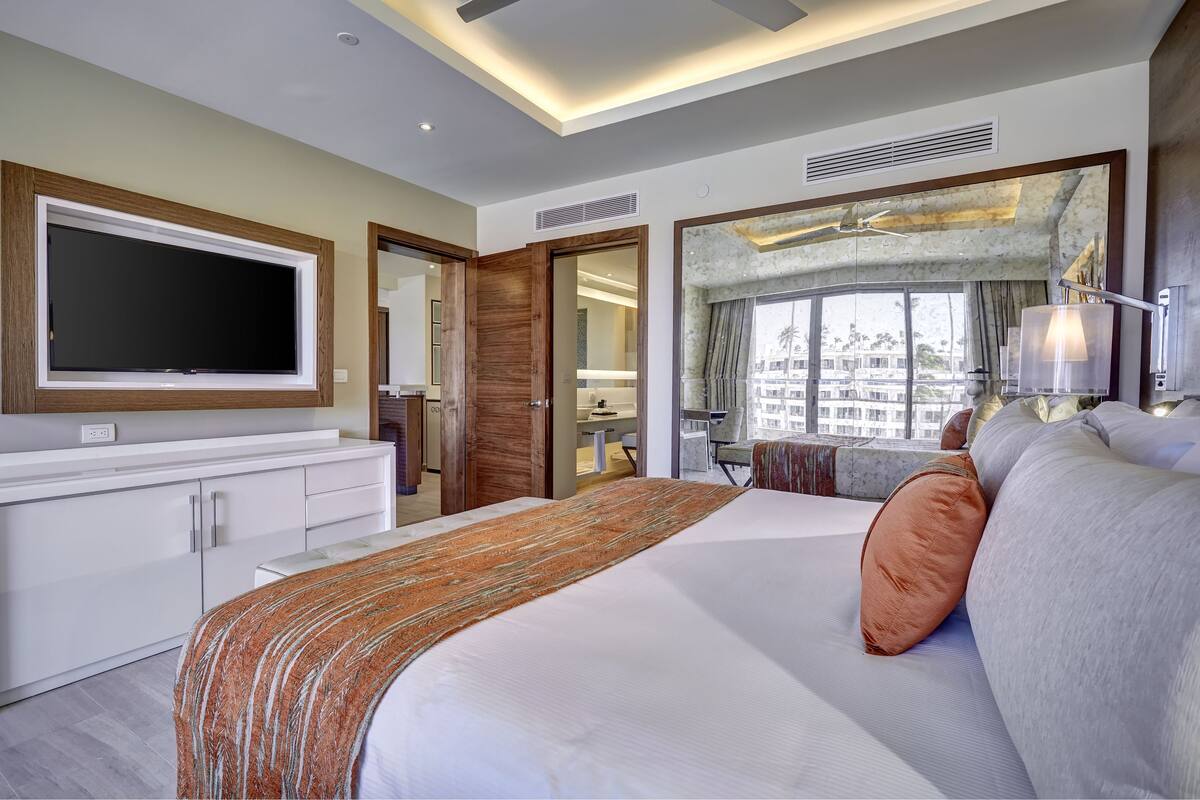 A modern hotel room with a large bed, a flat-screen TV, a walk-in closet, a bathroom, and a city view.