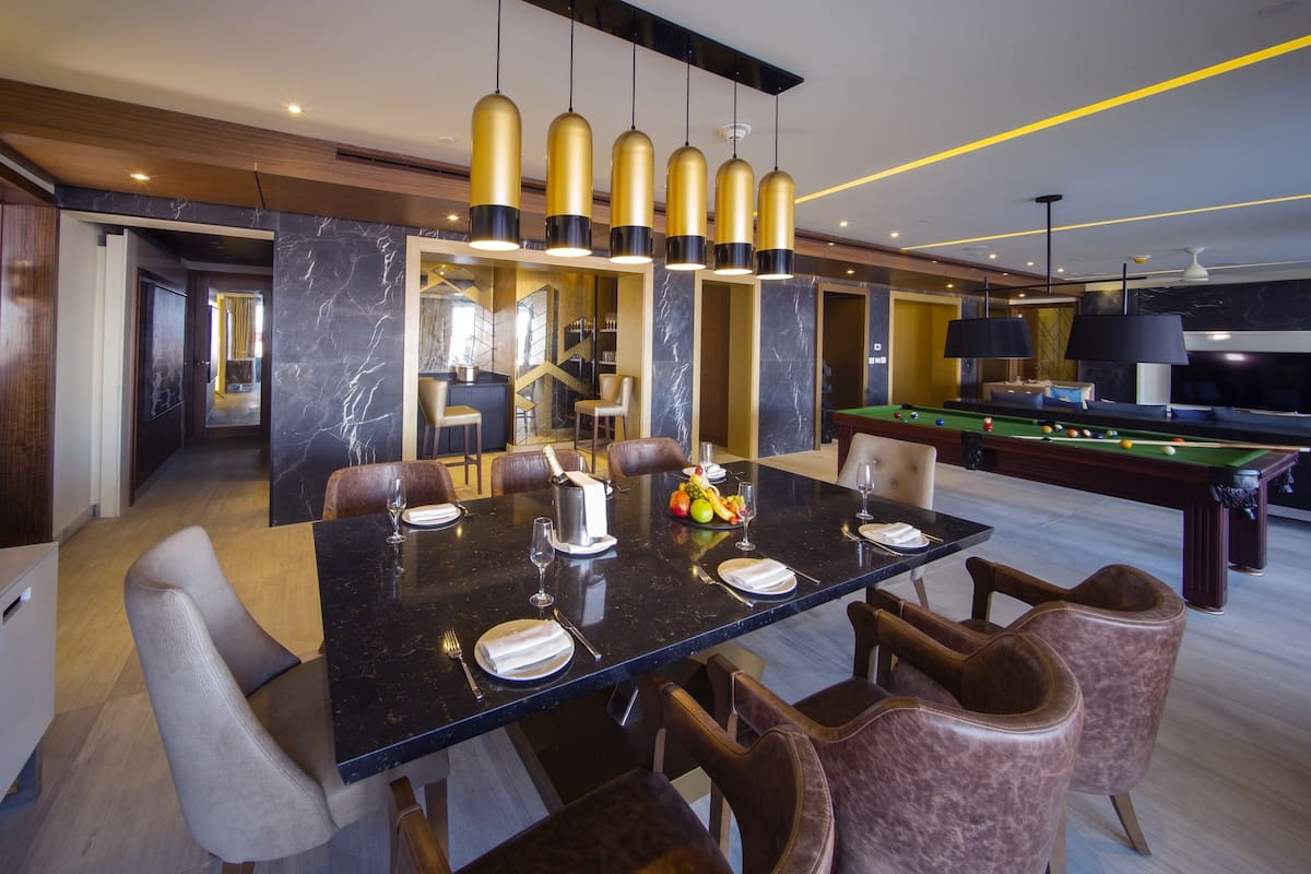 A modern dining area with a black marble table, gold pendant lights, and leather chairs.