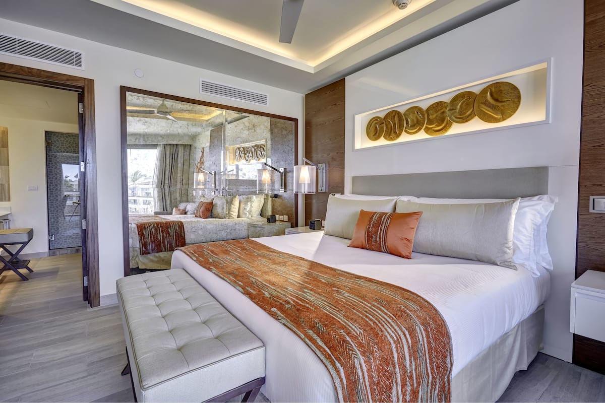 A modern hotel room with a large bed, a seating area, and a bathroom visible through an open door.