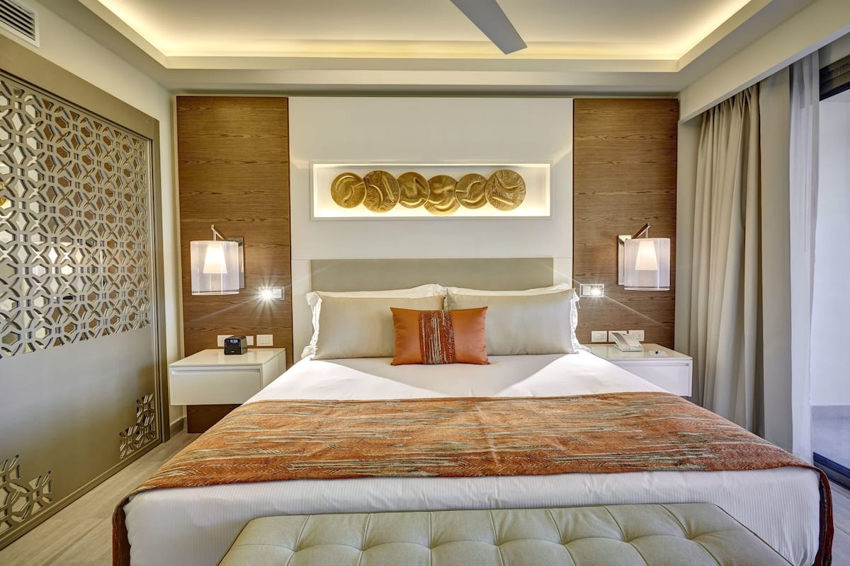 A modern hotel room with a large bed, decorative wall panels, and a ceiling fan.