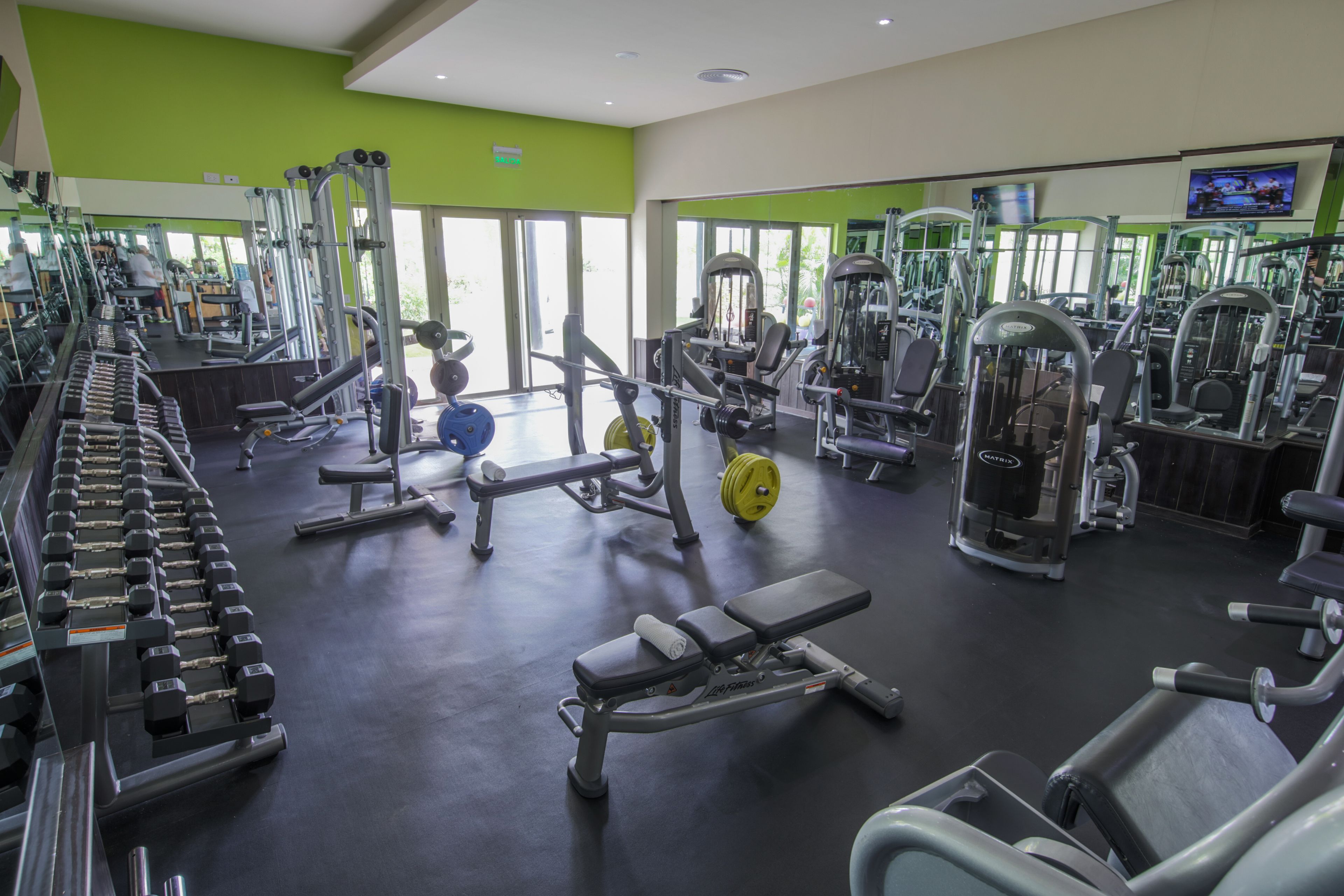 A gym with various exercise equipment, mirrors, and a television on the wall.