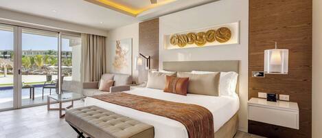 A modern hotel room with a large bed, a bench, a desk, and a view of the pool area.