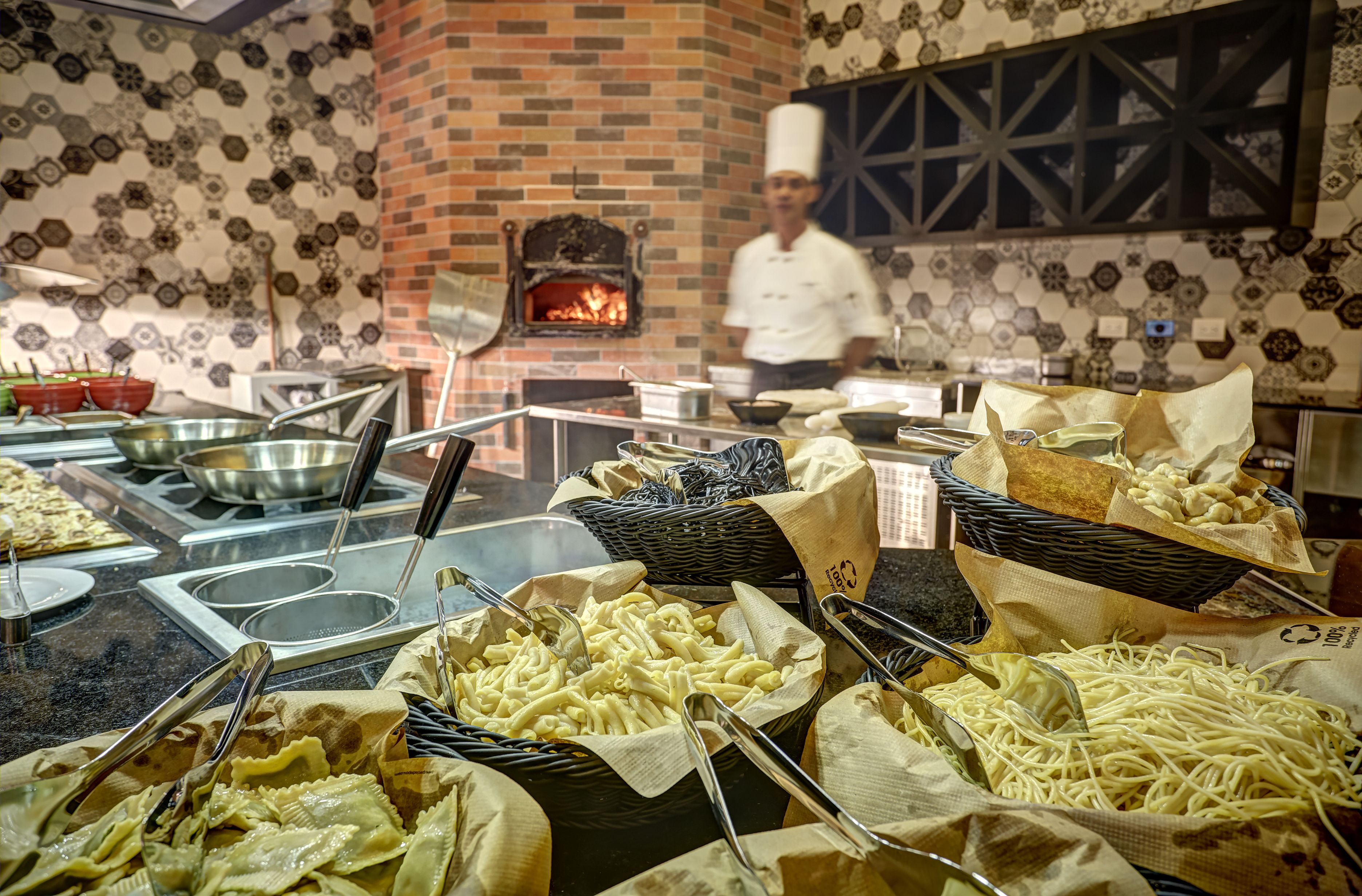 Un buffet con diversi primi piatti, un forno a mattoni sullo sfondo e uno chef in piedi.