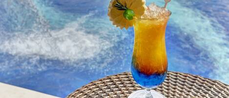 A cocktail with a layered effect, garnished with a lemon slice and a green sphere, on a glass with a coaster labeled "Riviera."