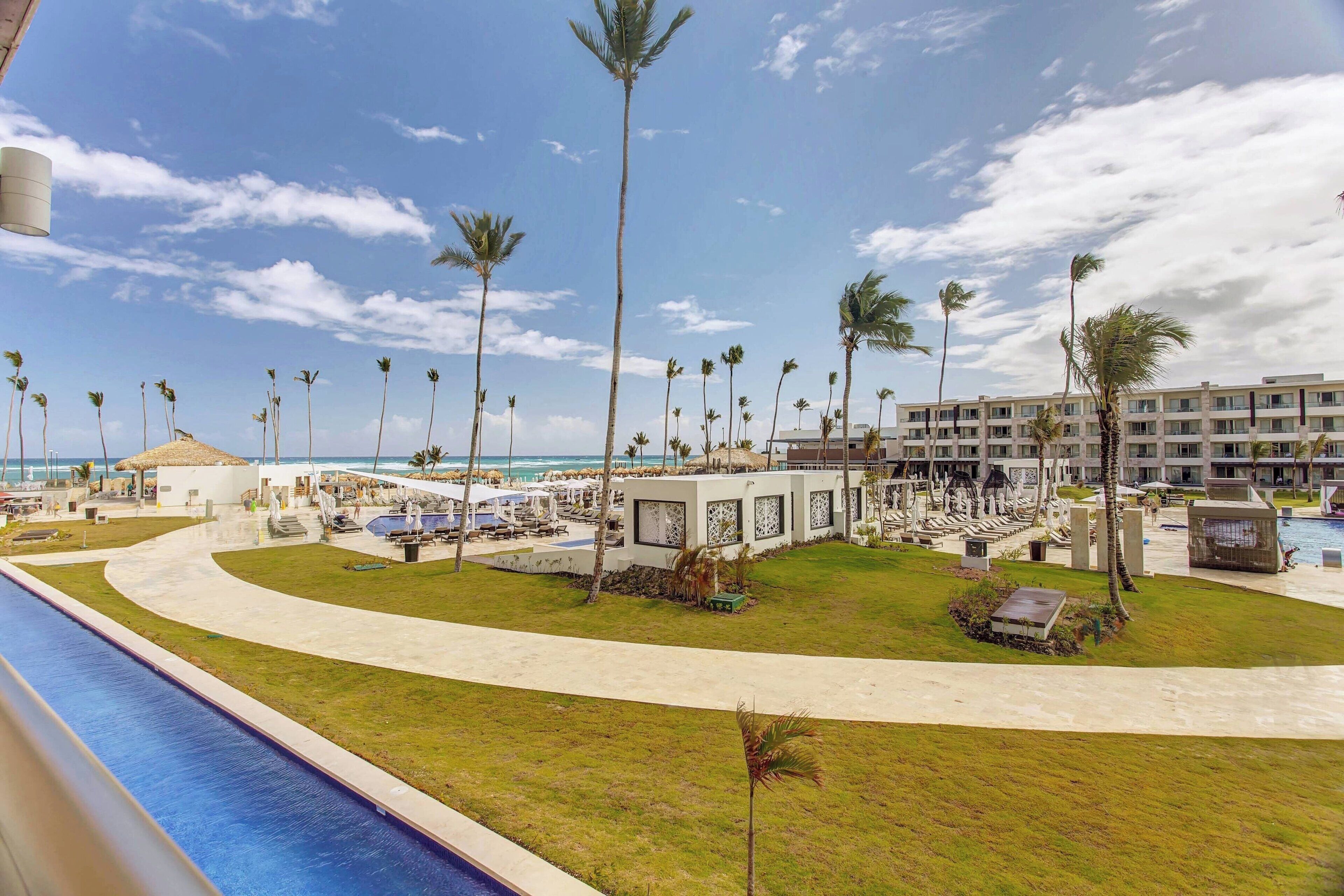 Un complexe hôtelier doté d’une piscine, de palmiers et offrant une vue sur la plage.