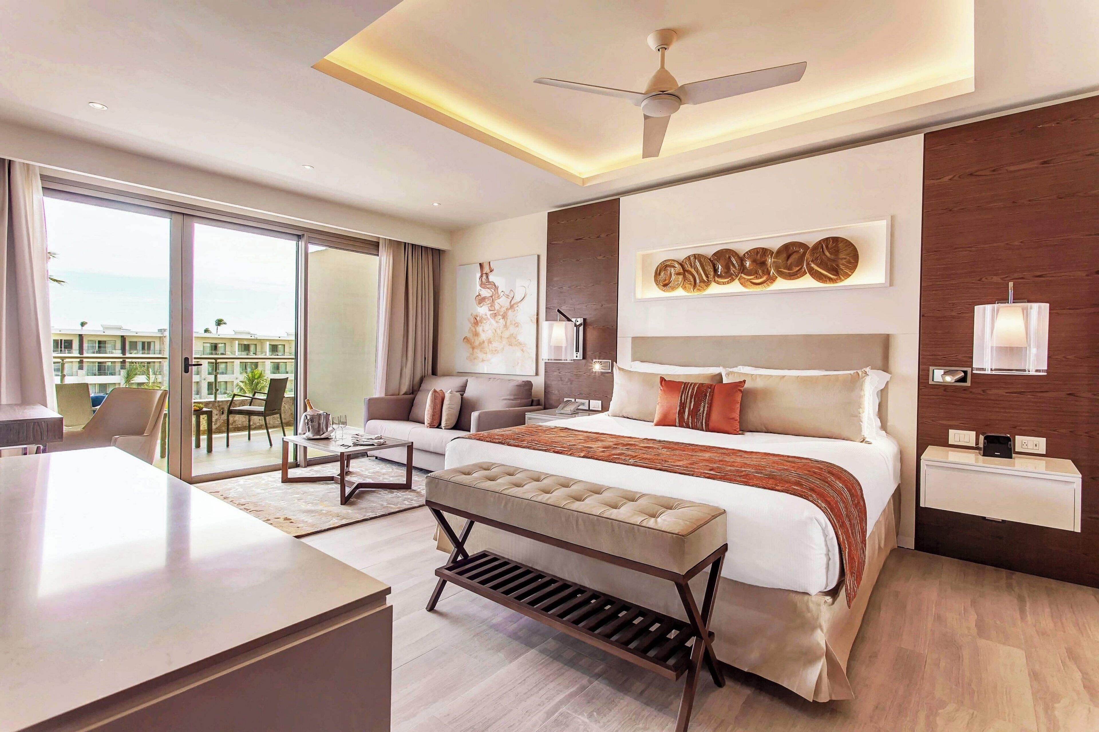 Una habitación de hotel moderna con una cama grande, un escritorio, un balcón con vistas y un ventilador de techo.