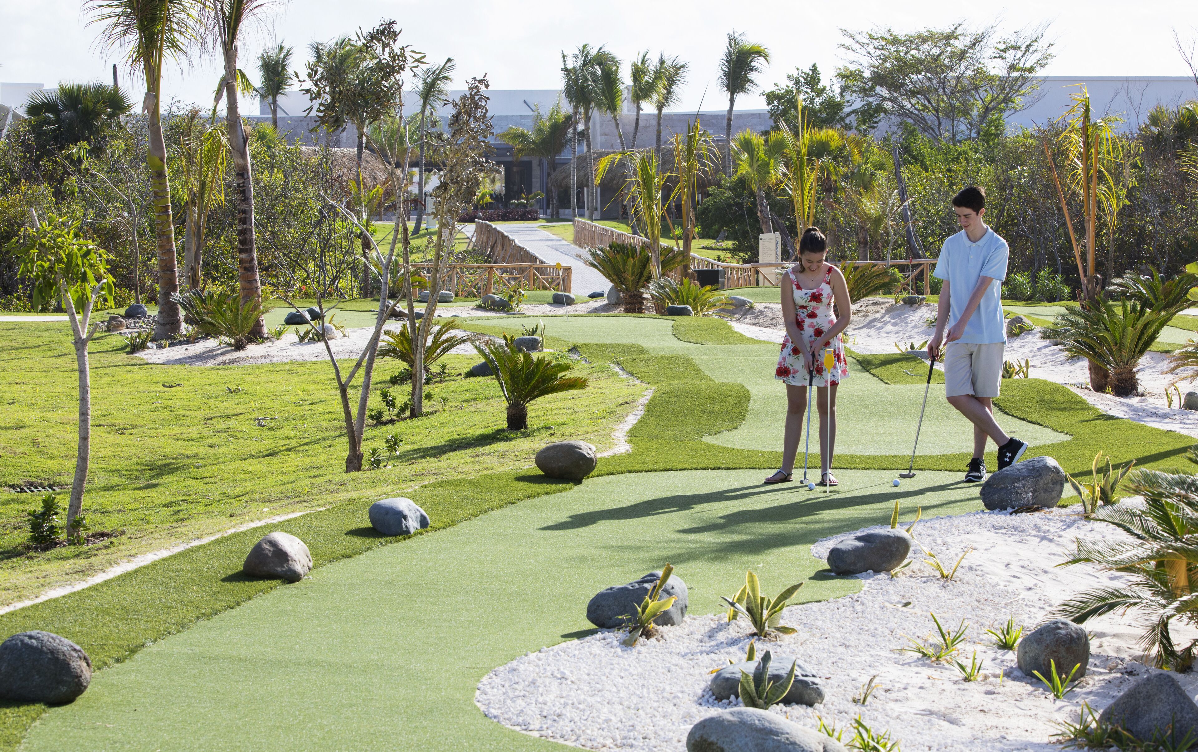 Un campo da golf con un green curato, bunker di sabbia e palme.