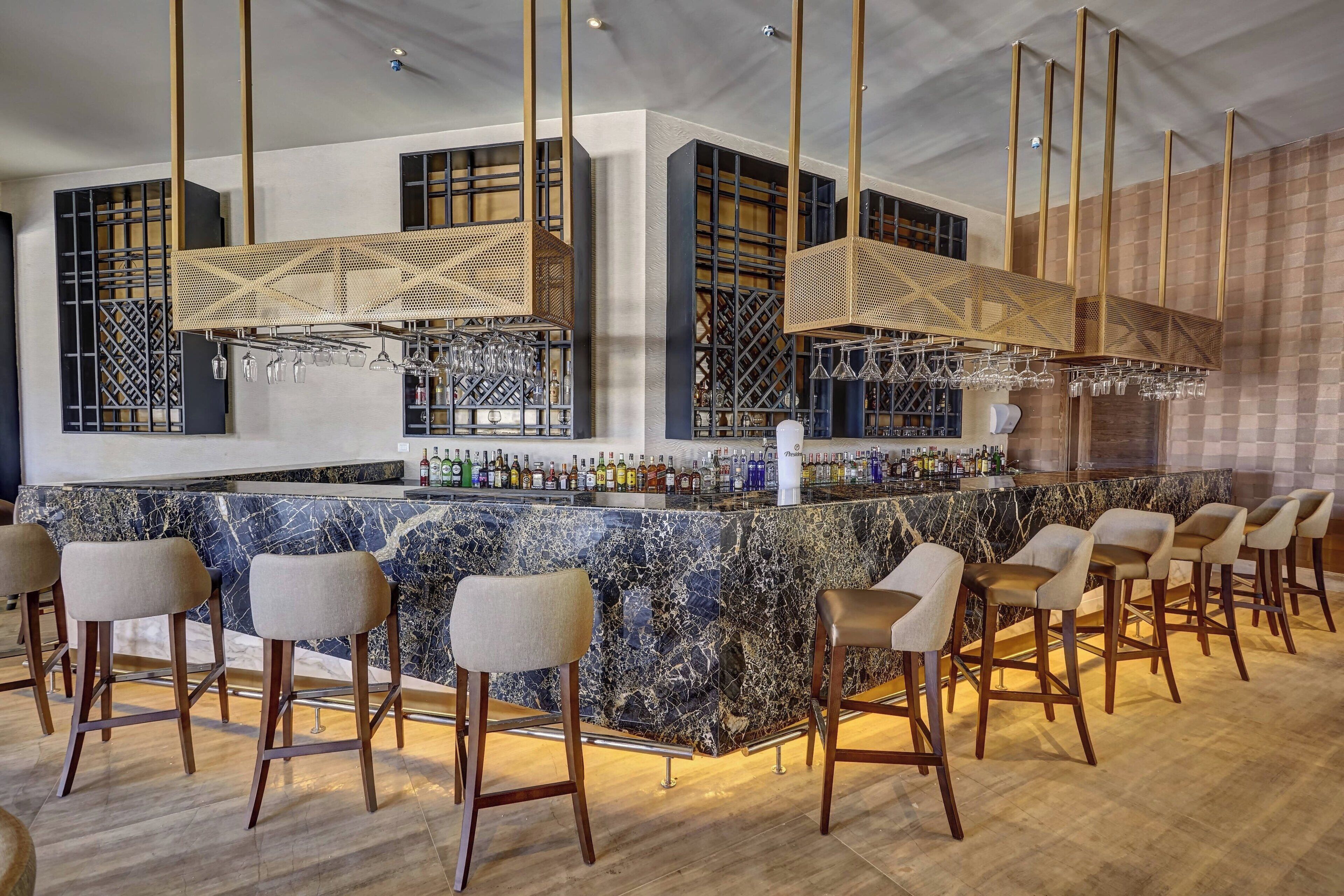 Eine Bar mit einer Marmorarbeitsplatte, mehreren Barhocker und hängenden Leuchten.