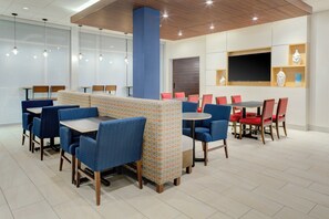 Um restaurante moderno com assentos em azul e vermelho, mesas de madeira e uma TV de tela plana na parede.